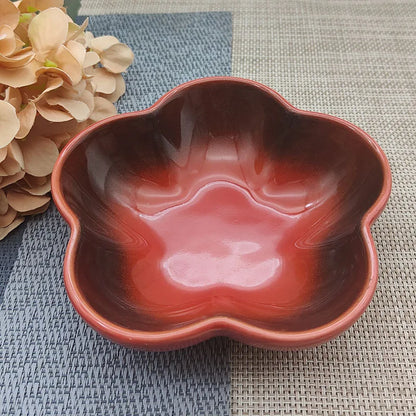 Gamelle pour chat en céramique rouge avec dégradé sombre en forme de fleur, design évasé et peu profond pour prévenir la fatigue des moustaches, présentée sur un tapis de table bicolore.