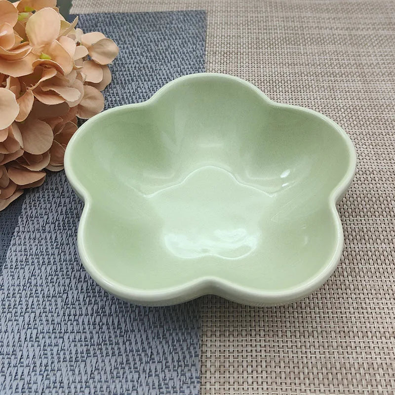 Gamelle pour chat en céramique vert amande brillant en forme de fleur, design évasé et peu profond pour prévenir la fatigue des moustaches, présentée sur un tapis de table texturé.