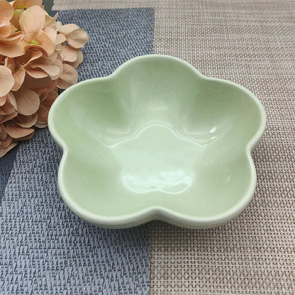 Gamelle pour chat en céramique vert amande brillant en forme de fleur, design évasé et peu profond pour prévenir la fatigue des moustaches, présentée sur un tapis de table texturé.