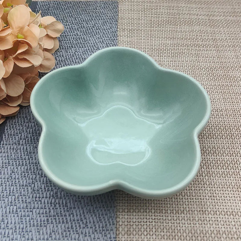 Gamelle pour chat en céramique vert menthe brillant en forme de fleur, design évasé et peu profond pour prévenir la fatigue des moustaches, présentée sur un tapis de table texturé.