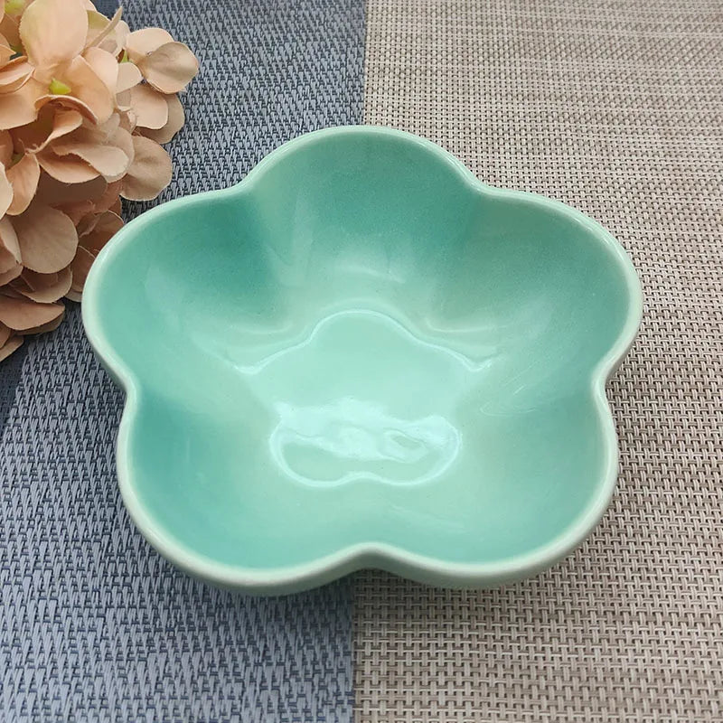 Gamelle pour chat en céramique vert menthe clair brillant en forme de fleur, design évasé et peu profond pour prévenir la fatigue des moustaches, présentée sur un tapis de table texturé.