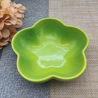 Gamelle pour chat en céramique vert pomme brillant en forme de fleur, design évasé et peu profond pour prévenir la fatigue des moustaches, présentée sur un tapis de table texturé.
