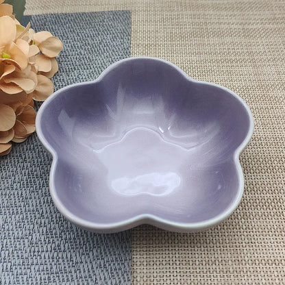 Gamelle pour chat en céramique violette brillante en forme de fleur, design évasé et peu profond pour prévenir la fatigue des moustaches, présentée sur un tapis de table bicolore.
