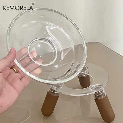 Main tenant un bol en verre transparent amovible au-dessus de son support trépied design, illustrant la facilité d'entretien de la gamelle surélevée Kemorela pour chat.