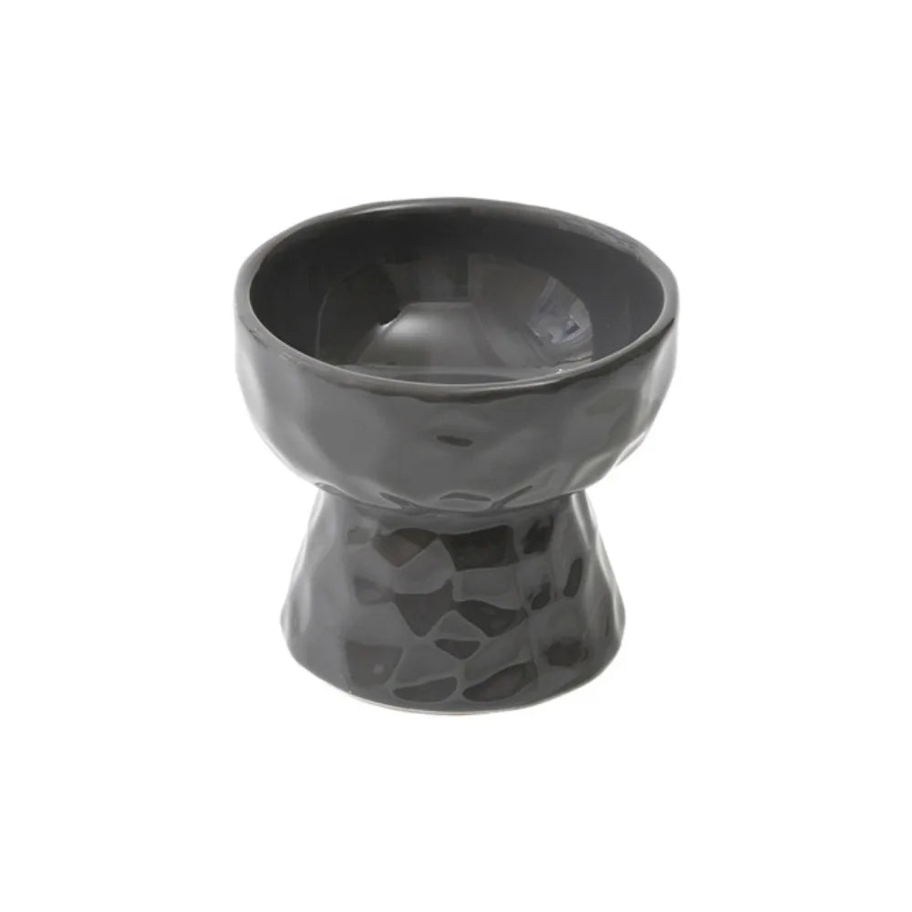Gamelle pour chat surélevée en céramique noire avec texture martelée facettée et fini brillant. Cette gamelle animaux ergonomique et inclinée protège les cervicales et facilite la digestion de votre félin. Une gamelle chat design et hygiénique, idéale pour une alimentation saine et un intérieur moderne.