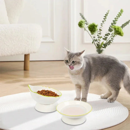 Chat gris dégustant ses croquettes dans une gamelle pour chat surélevée en céramique blanche au design tête de chat. Cet ensemble de gamelle chat ergonomique avec liseré vert et fond rose assure un confort digestif optimal. Une gamelle de luxe stable et élégante pour un intérieur moderne.