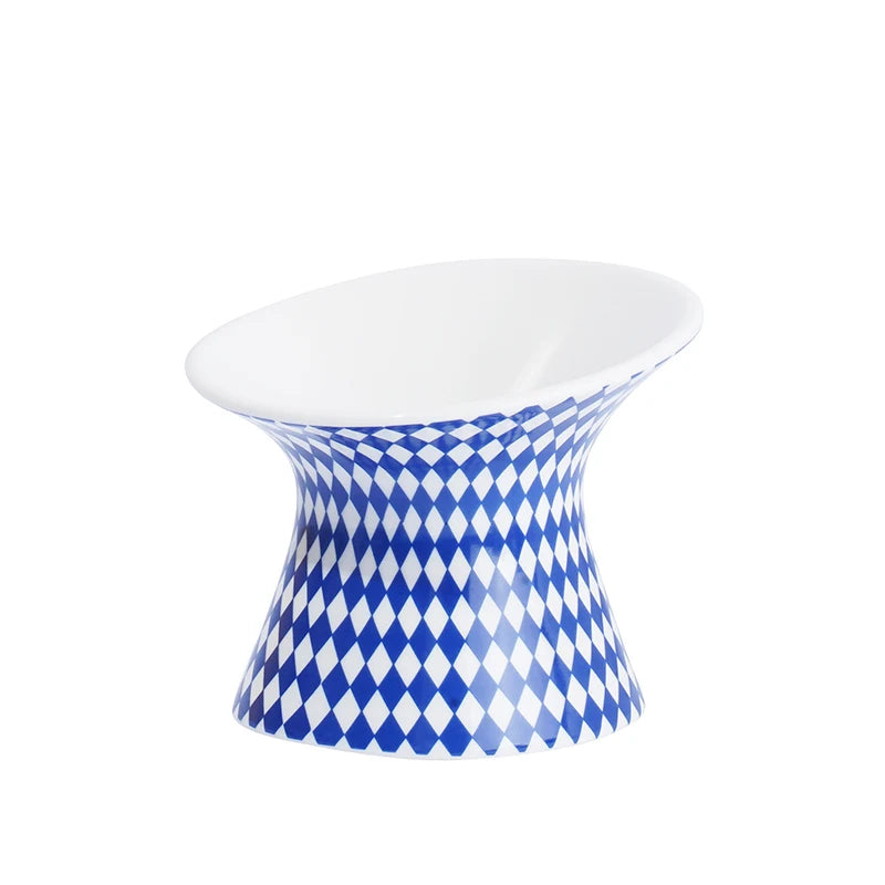 Gamelle pour chat surélevée en céramique blanche et bleue à motifs losanges arlequin. Cette gamelle animaux ergonomique et inclinée protège les cervicales et facilite la digestion de votre félin. Une gamelle pour chat haut de gamme, stable, hygiénique et design, idéale pour un intérieur moderne et le confort de votre animal.