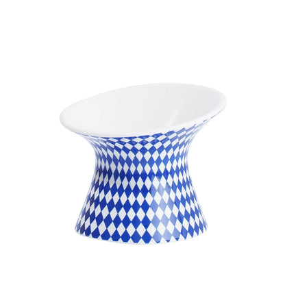 Gamelle pour chat surélevée en céramique blanche et bleue à motifs losanges arlequin. Cette gamelle animaux ergonomique et inclinée protège les cervicales et facilite la digestion de votre félin. Une gamelle pour chat haut de gamme, stable, hygiénique et design, idéale pour un intérieur moderne et le confort de votre animal.