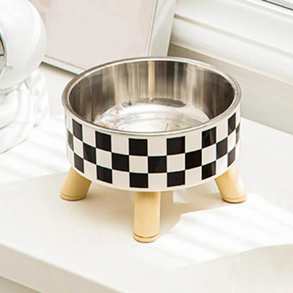 Gamelle pour chat surélevée avec bol en acier inoxydable et support trépied en bois clair au design damier noir et blanc. Cette gamelle chat orthopédique de luxe assure un confort cervical optimal et une hygiène parfaite contre l'acné du menton. Une gamelle robuste et élégante au style scandinave pour le bien-être de votre félin.