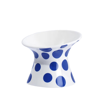 Gamelle pour chat surélevée et inclinée en céramique blanche à pois bleus. Cette gamelle animaux ergonomique prévient les douleurs cervicales et facilite la digestion grâce à son design orthopédique. Une gamelle pour chat de luxe, hygiénique et stable, idéale pour un intérieur moderne et le confort de votre félin.