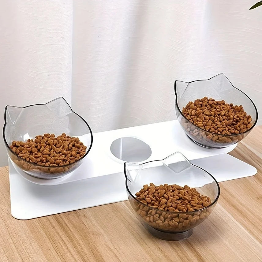 Station de repas triple avec gamelle pour chat modulable. Le visuel montre deux bols transparents sur un support blanc incliné à 15 degrés et un bol posé au sol. Cette gamelle chat ergonomique protège les cervicales et facilite la digestion. Un ensemble gamelle chaton au design d'oreilles de chat, idéal pour séparer l'eau et la nourriture avec style.