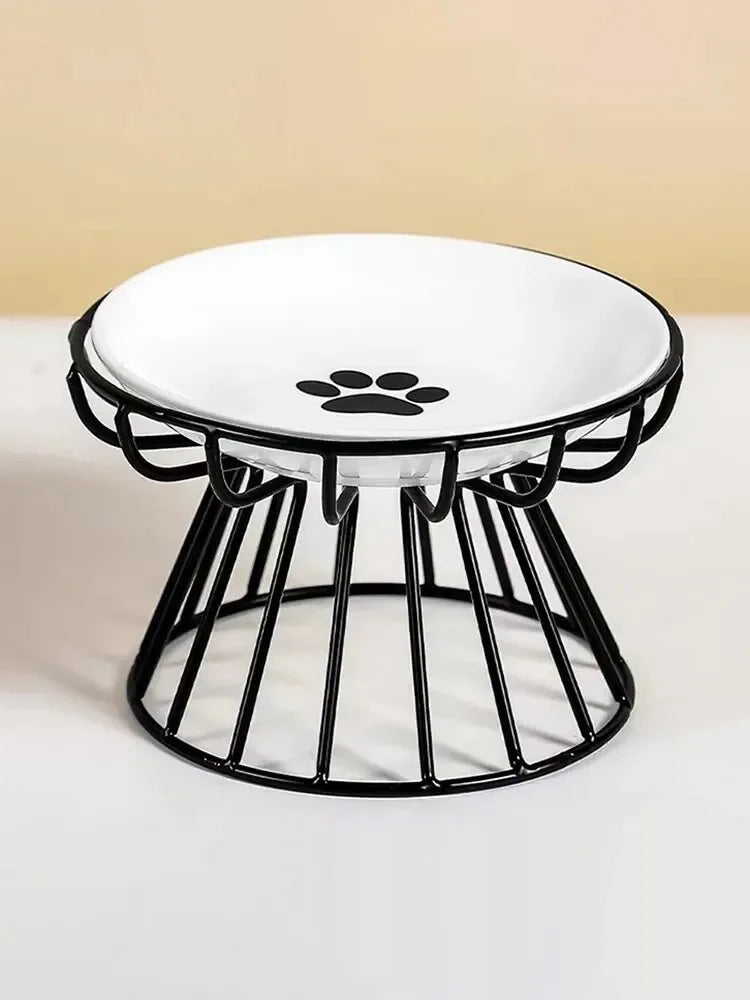 Gamelle surélevée pour chat avec bol en céramique blanche orné d'un motif patte noire, posé sur un support ergonomique en métal noir au design moderne et stable.