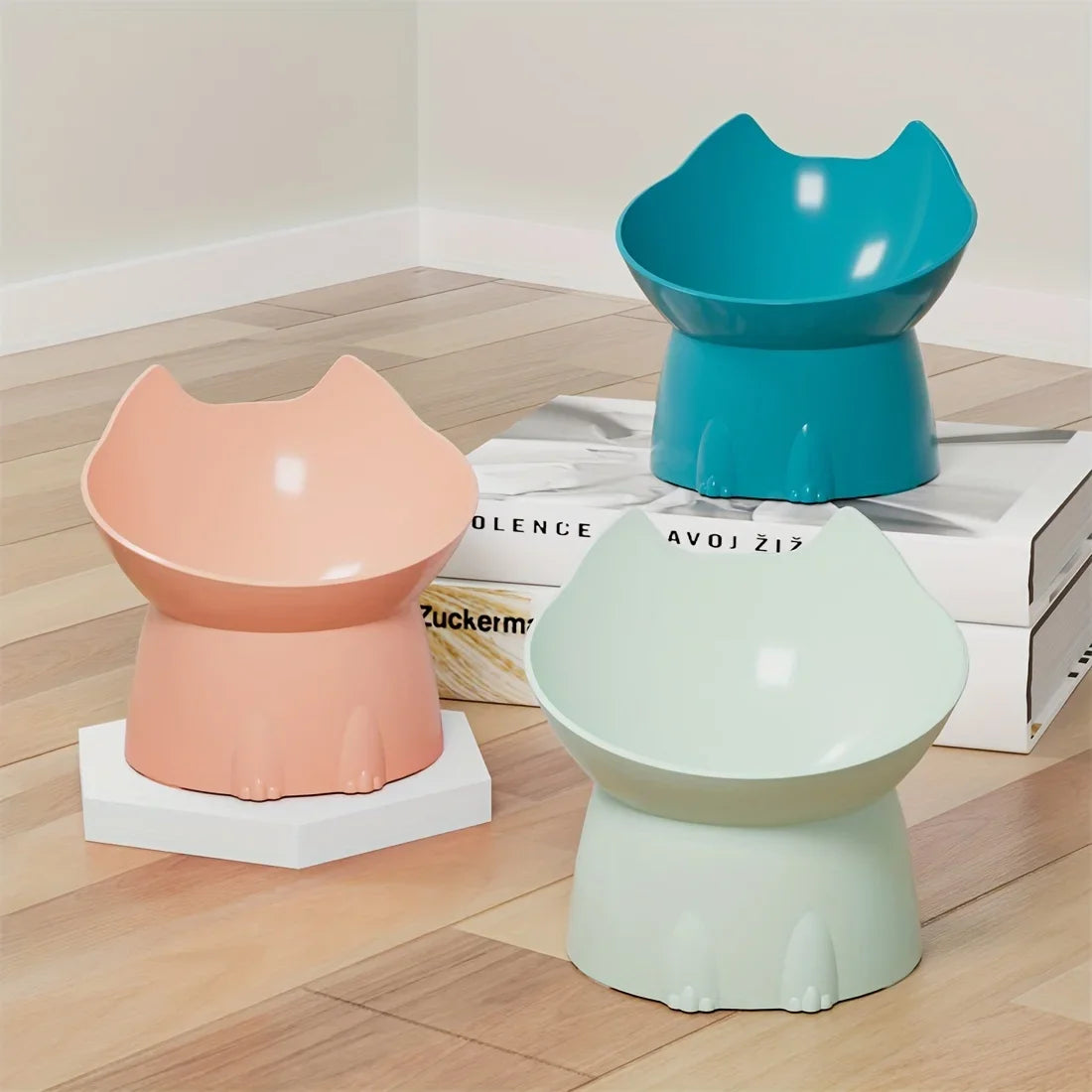 Trio de gamelles surélevées pour chat au design ergonomique avec oreilles de chat, présentées en coloris corail, bleu turquoise et vert menthe dans un intérieur moderne.