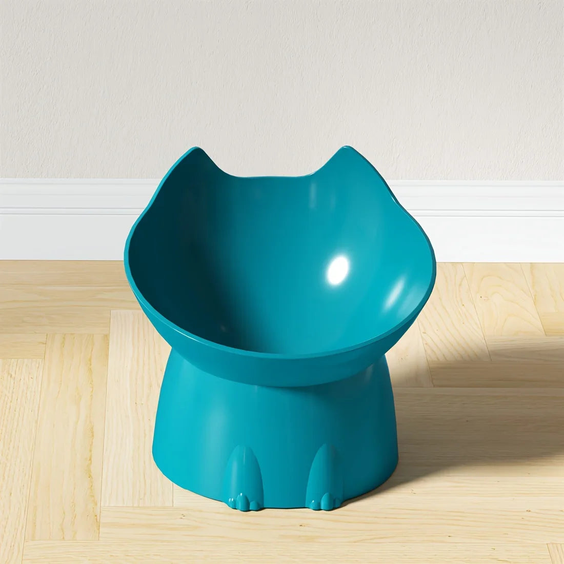 Gamelle surélevée pour chat au design ergonomique bleu turquoise, bol incliné en forme de tête de chat avec oreilles, posé sur un parquet clair devant un mur blanc.