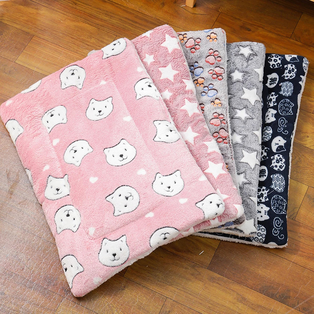 Éventail de plusieurs modèles de tapis chat en peluche épaisse avec motifs étoiles, pattes et têtes de chats. L'image présente ce coussin à chat disponible en rose, gris et bleu marine sur un sol en bois. Coussin pour chat matelassé, chaud et ultra-doux pour l'hiver. Qualité premium Les Trésors d'Owka.