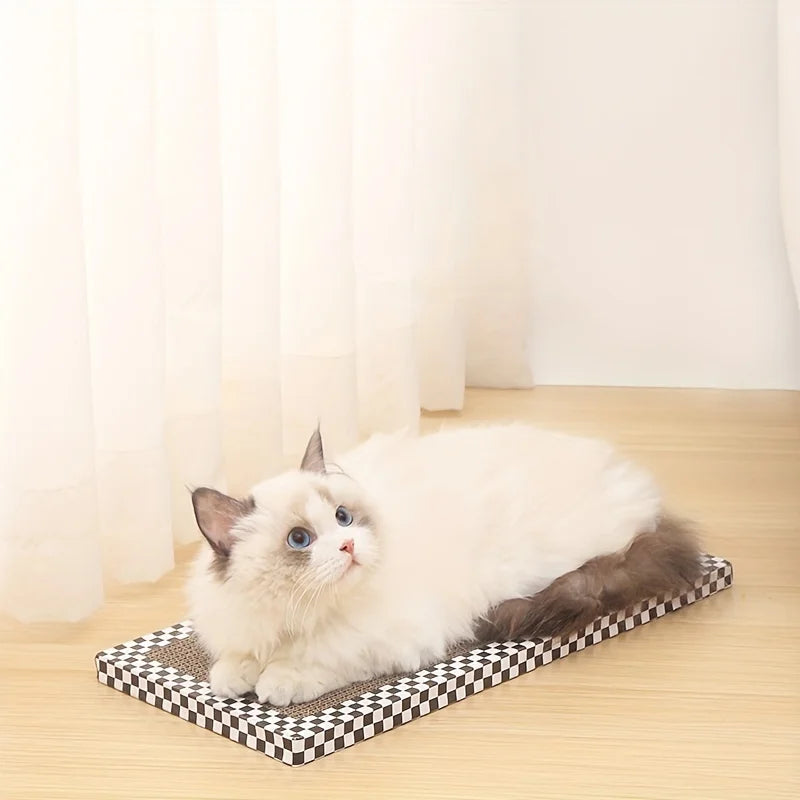 Chat blanc à poils longs allongé sur une planche à griffer rectangulaire en carton ondulé avec bordure à damier noir et blanc, posée sur un sol clair devant un rideau blanc.