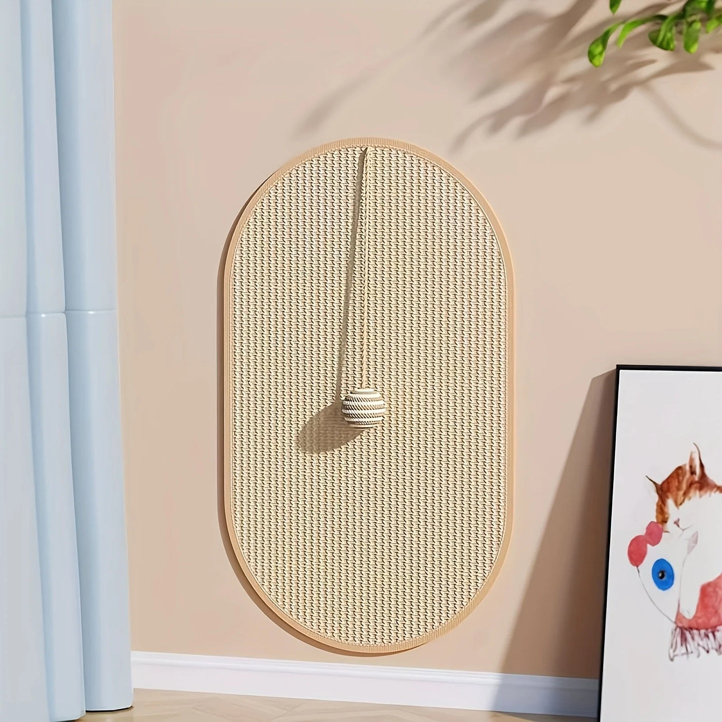 Griffoir chat mural design en sisal tressé de forme ovale. Vue de face d'un griffoir pour chat avec balle de jeu suspendue et cadre en bois clair. Griffoir sisal chat Les Trésors d'Owka, accessoire de protection murale élégant pour décoration intérieure moderne.