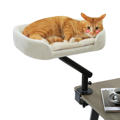 Hamac à chat bureau ergonomique avec fixation rotative. Ce hamac pour chat en peluche blanche se fixe sur le rebord d'une table pour laisser votre félin dormir près de vous. Un hamac chat robuste et confortable, idéal pour le télétravail avec son chat roux.