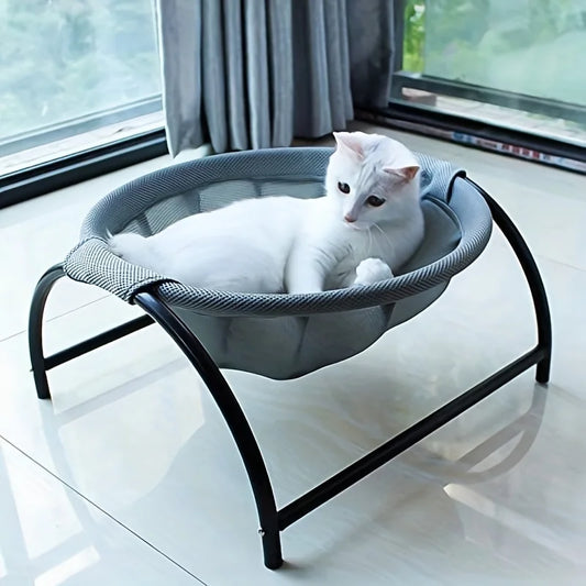 Hamac chat surélevé avec structure design en métal noir et nacelle en tissu mesh gris respirant. L'image montre un chat blanc profitant de ce coussin à chat suspendu près d'une fenêtre. Alternative moderne au coussin pour chat classique, offrant une ventilation naturelle et un confort ergonomique. Qualité Les Trésors d'Owka.