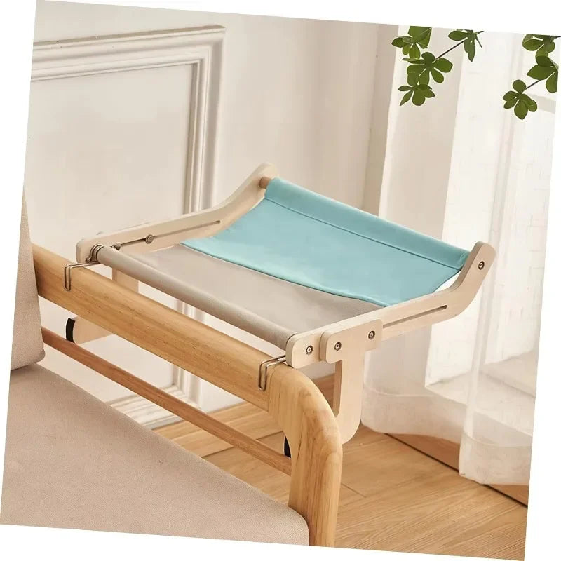 Hamac pour chat en bois naturel avec assise en toile bleue et grise, fixé sur le dossier d'un canapé. L'image montre le système d'accroche universel sans perçage pour hamac chaton de luxe. Mobilier de repos stable, esthétique et robuste pour hamac a chat de salon. Qualité premium Les Trésors d'Owka.