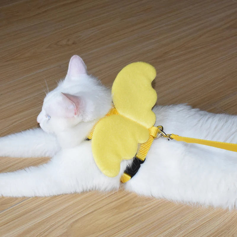 Chat blanc allongé portant un harnais pour chat avec des ailes d'ange jaune vif en peluche. Ce harnais chat ajustable en nylon jaune est vendu avec sa laisse assortie. Un accessoire de type harnais animaux original, confortable et sécurisé, idéal pour les propriétaires cherchant un design mignon et unique pour les balades en extérieur.