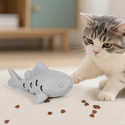 Chat tigré jouant avec un jouet chat en forme de poisson gris distributeur de friandises. Ce jeux interactif chat en silicone stimule l'instinct de chasse et distribue des croquettes pour une occupation mentale saine. Un incontournable des jeux animaux pour lutter contre l'ennui et l'obésité féline.