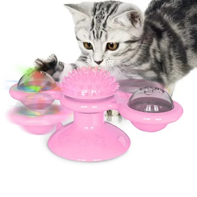 Jouet interactif rose pour chat en forme de moulin à vent avec ventouse, doté d'une boule de massage centrale et de deux globes rotatifs contenant des billes lumineuses, présenté avec un chaton gris en plein jeu.