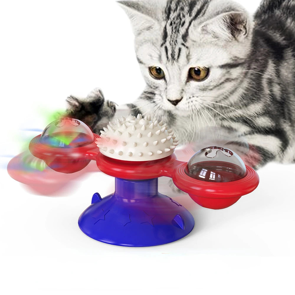 Jouet interactif tricolore (rouge, bleu et blanc) pour chat en forme de moulin à vent avec ventouse, doté d'une boule de massage centrale et de deux globes rotatifs contenant des billes lumineuses, présenté avec un chaton gris.