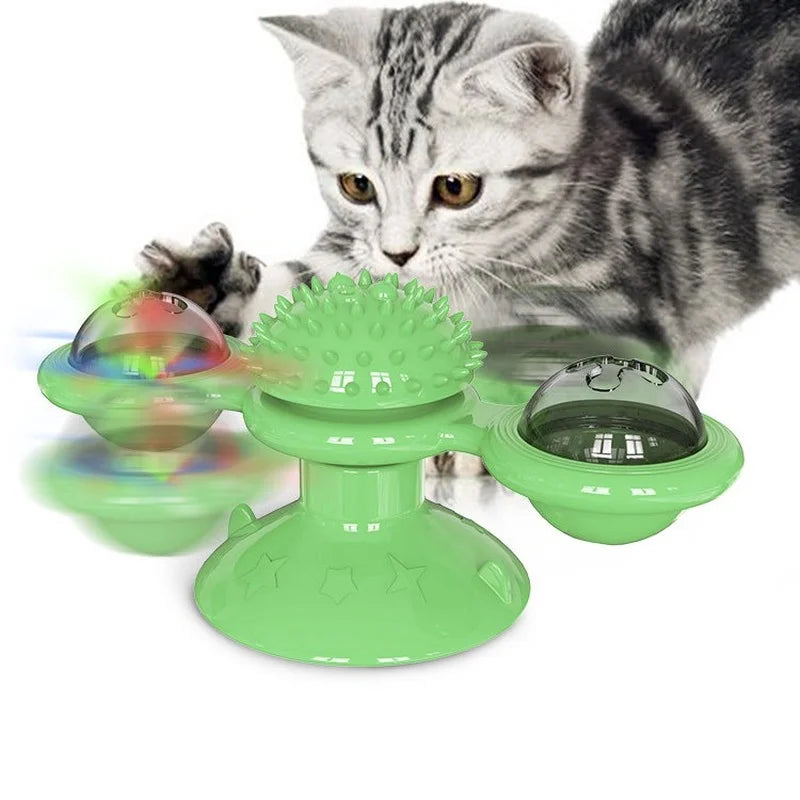 Jouet interactif vert pour chat en forme de moulin à vent avec ventouse, doté d'une boule de massage centrale et de deux globes rotatifs contenant des billes lumineuses, présenté avec un chaton gris en plein jeu.