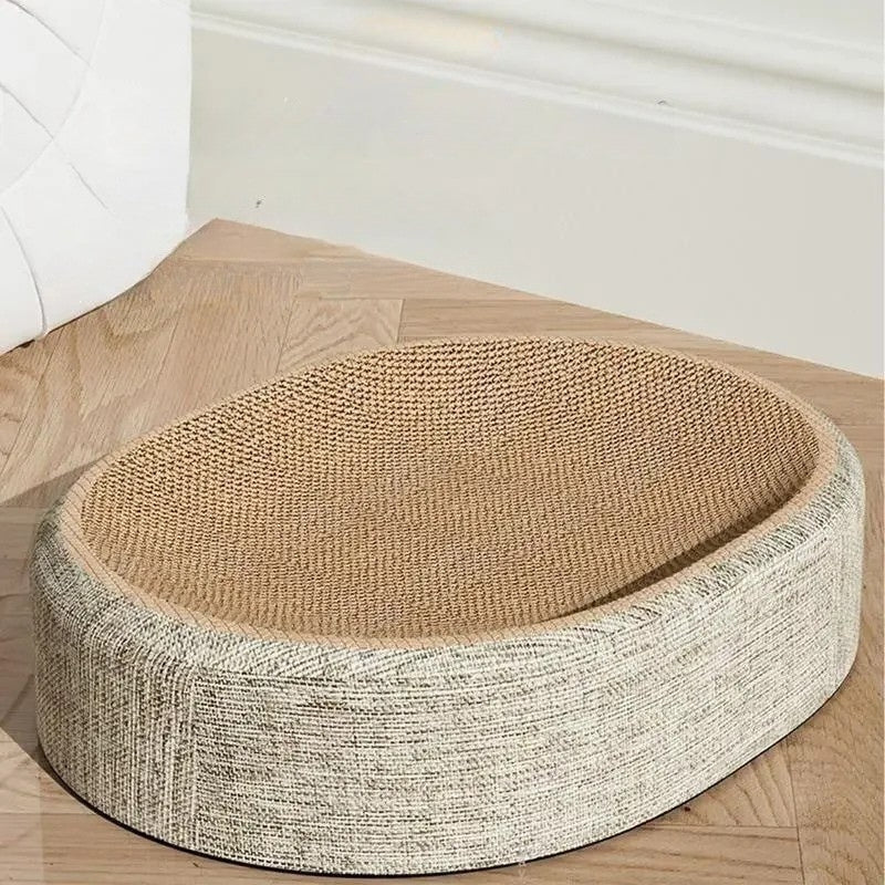 Panier griffoir pour chat de forme ovale avec surface incurvée en carton ondulé haute densité et contour en tissu beige chiné, posé sur un parquet en chevrons.