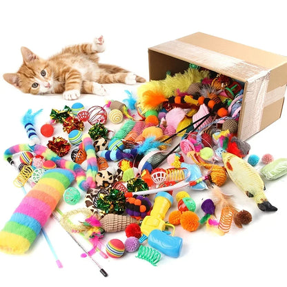 Un grand carton ouvert déversant une multitude de jouets multicolores pour chat (balles, souris, plumes, ressorts, tunnels) à côté d'un chaton roux allongé sur le dos.
