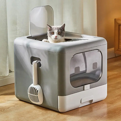 Un chat gris et blanc sortant par l'ouverture supérieure d'un bac à litière chat gris et blanc au design cubique. Cette maison de toilette fermée inclut une porte frontale transparente, une pelle latérale et une grille de toit, parfait comme bac à litière pour chaton.