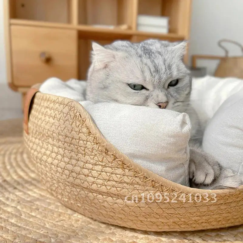 Chat gris installé dans un panier rond en corde tressée beige, utilisant le rebord abaissé et le coussin moelleux blanc comme appui-tête pour un sommeil confortable.