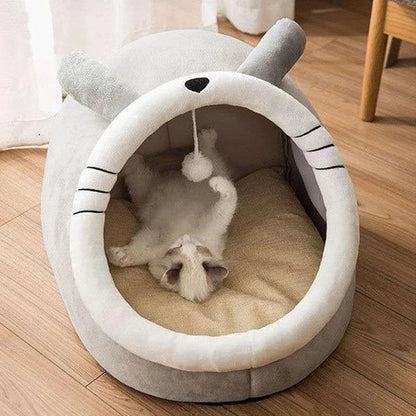 Panier chat en forme de dôme gris avec oreilles et moustaches brodées. L'image montre un chaton couché sur le dos dans ce coussin à chat igloo ultra-moelleux avec pompon de jeu suspendu. Lit fermé protecteur et amusant pour petit animal, parfait comme coussin pour chat cocooning. Qualité Les Trésors d'Owka.