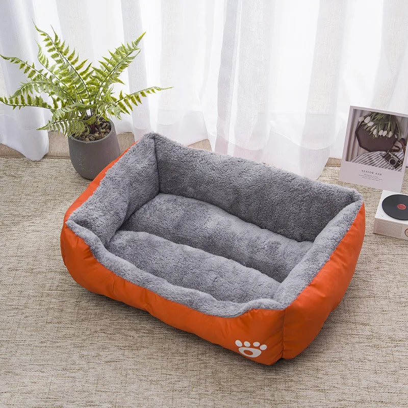 Panier chat rectangulaire orange et gris avec intérieur en peluche épaisse. L'image présente ce coussin pour chat bicolore avec rebords rembourrés et logo patte dans un salon lumineux. Lit douillet, spacieux et isolant pour un confort de type coussin a chat. Qualité premium Les Trésors d'Owka.