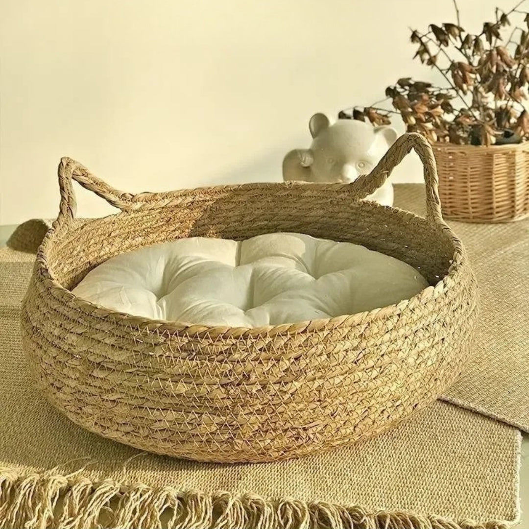 Panier pour chat rond en osier tressé naturel avec poignées en forme d'oreilles de chat, incluant un coussin blanc capitonné ultra-moelleux sur un tapis de jute.