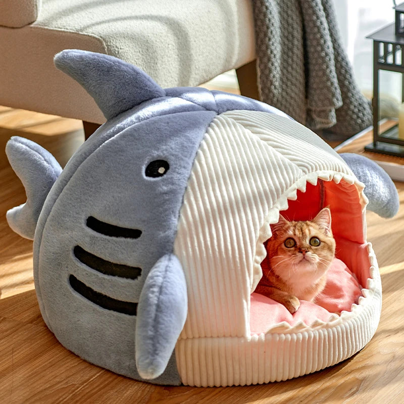Panier chat en forme de requin avec gueule ouverte, dents décoratives et nageoires. L'image montre un chaton roux allongé sur le coussin pour chat intérieur rose de cette niche igloo. Lit original, chaud et ludique pour un confort type coussin a chat. Qualité Les Trésors d'Owka.