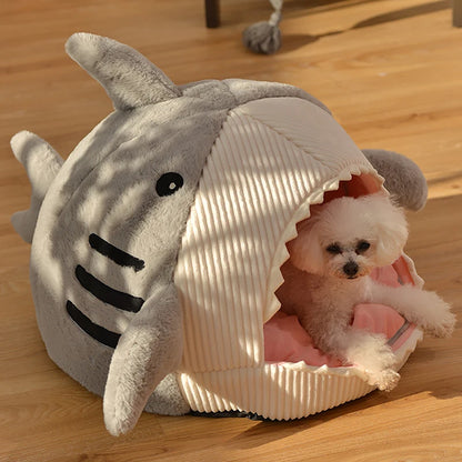 Panier chat original en forme de requin gris avec nageoires et dents. L'image montre un petit chien dans cette niche igloo équipée d'un coussin pour chat intérieur rose moelleux. Lit design, chaud et protecteur en velours côtelé pour un confort type coussin a chat. Qualité Les Trésors d'Owka.