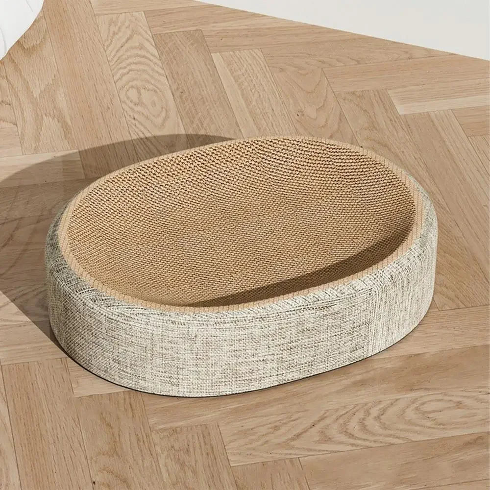 Lit griffoir pour chat de forme ovale avec surface de griffage incurvée en carton ondulé haute densité et revêtement extérieur en tissu beige chiné, posé sur un parquet en chevrons.