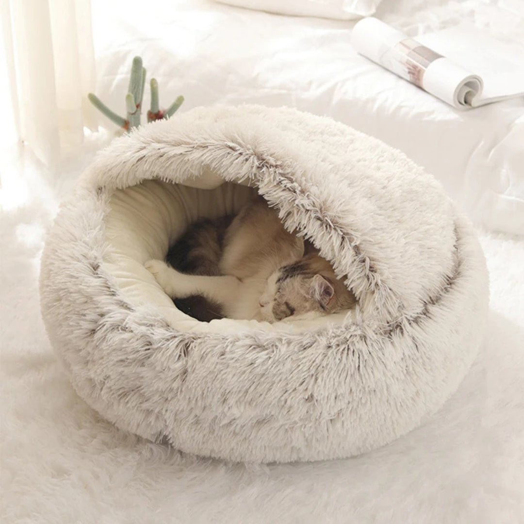 Chat endormi paisiblement à l'intérieur d'un panier grotte apaisant beige crème en peluche shaggy ultra-douce, avec toit protecteur souple pour un confort thermique optimal.