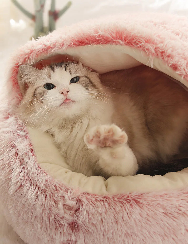 Chaton installé confortablement dans son panier grotte apaisant en peluche rose et blanche, montrant le toit protecteur souple et l'intérieur moelleux idéal pour réduire l'anxiété.