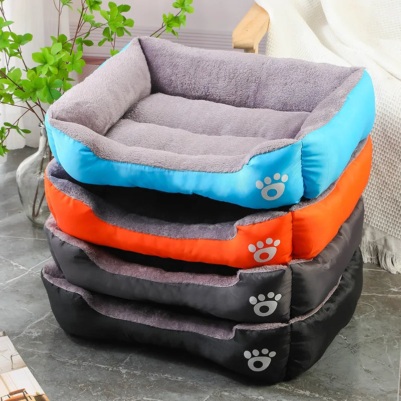 Pile de paniers chat bicolores avec intérieur en peluche grise douce. L'image montre quatre coloris (bleu, orange, noir, gris) de ce coussin pour chat rectangulaire avec motif patte. Lit confortable et résistant pour coussin a chat. Qualité premium Les Trésors d'Owka.