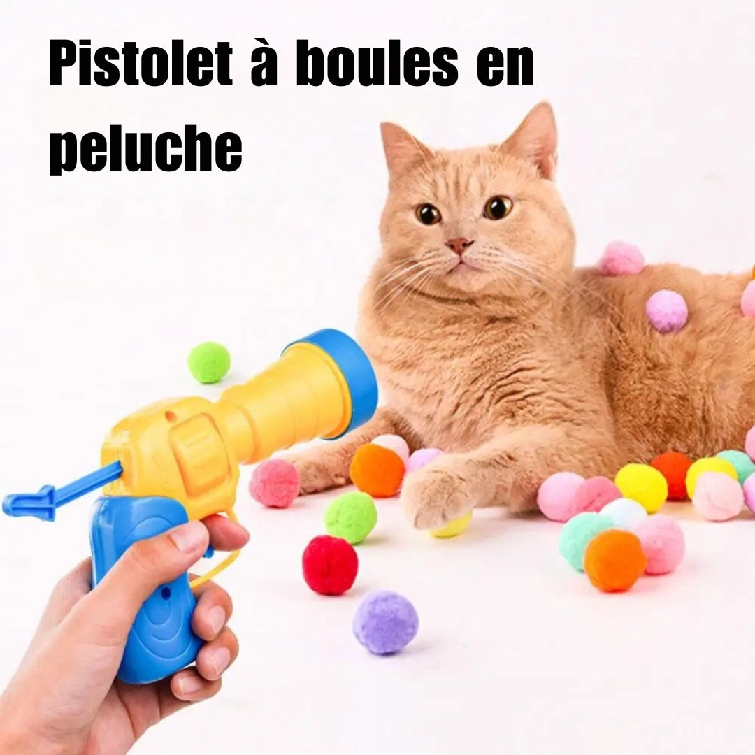 Jouet interactif pour chat comprenant un pistolet lanceur jaune et bleu tenu en main, entouré de nombreuses balles en peluche multicolores éparpillées autour d'un chat roux.