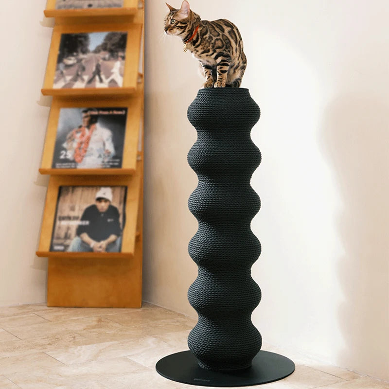 Chat Bengal assis au sommet d'un haut poteau à griffer sculptural noir en forme de colonne ondulée, fabriqué en corde tressée sur une base circulaire stable.