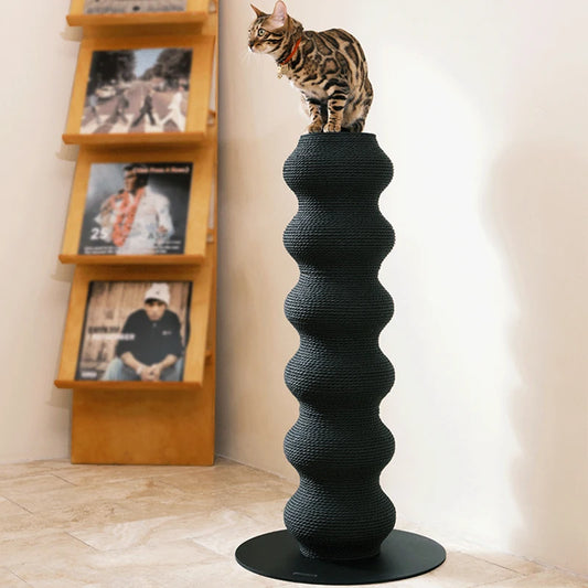 Chat Bengal assis au sommet d'un haut poteau à griffer sculptural noir en forme de colonne ondulée, fabriqué en corde tressée sur une base circulaire stable.