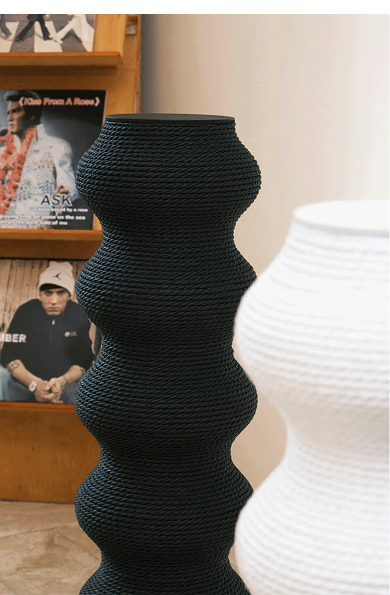 Comparaison de deux hauts poteaux à griffer sculpturaux pour chat en forme de colonnes ondulées, l'un en corde noire et l'autre en blanc, présentés dans un salon au style moderne.