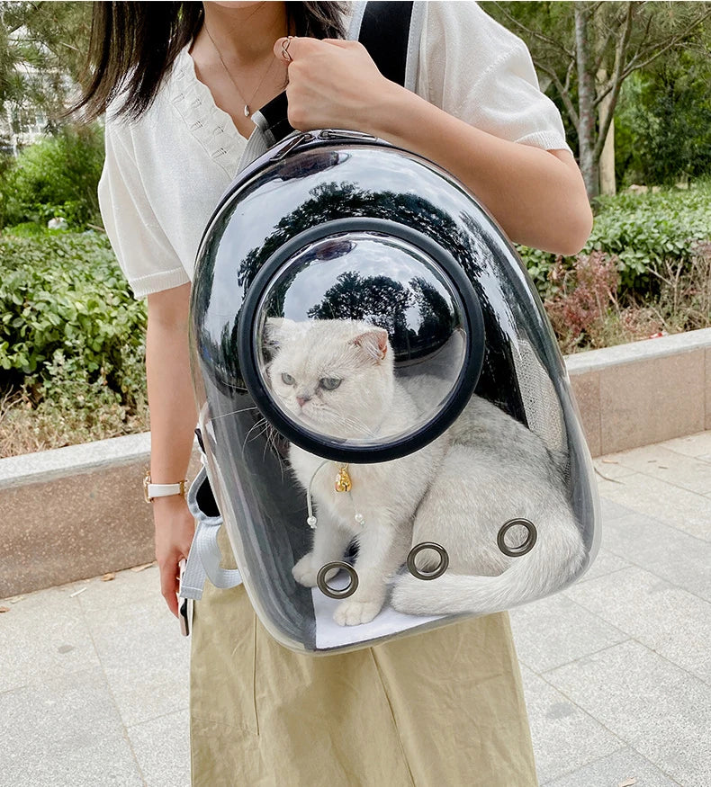 Femme portant à l'épaule un sac à dos de transport pour chat noir avec une grande fenêtre panoramique transparente, montrant un chat blanc serein à l'intérieur profitant de la vue extérieure.