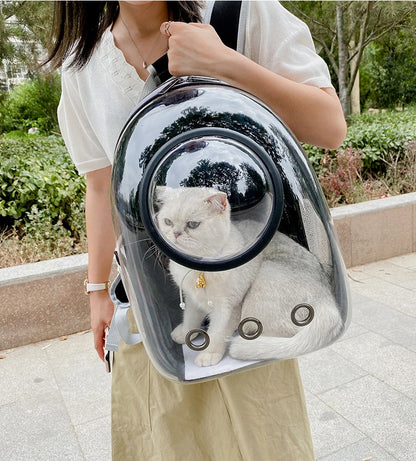 Femme portant à l'épaule un sac à dos de transport pour chat noir avec une grande fenêtre panoramique transparente, montrant un chat blanc serein à l'intérieur profitant de la vue extérieure.