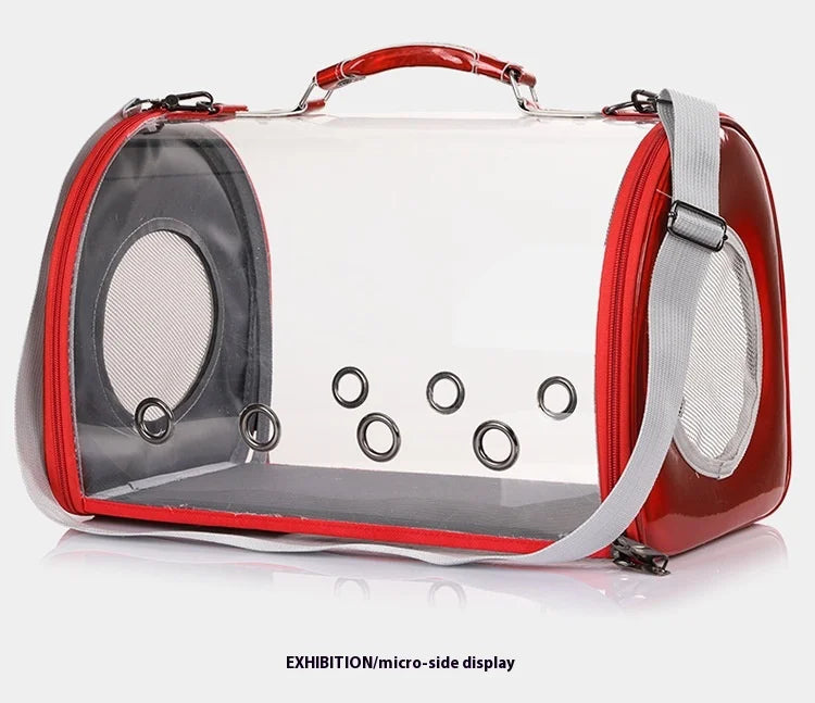 Sac de transport panoramique pour chat et petit chien en matériau transparent rigide avec finitions rouge brillant, équipé de six œillets de ventilation frontaux, d'une poignée ergonomique et d'une bandoulière grise.