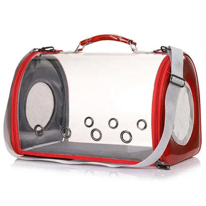 Sac de transport panoramique pour chat et petit chien en matériau transparent rigide avec finitions rouge irisées, équipé de six œillets de ventilation frontaux et d'une poignée de portage ergonomique.